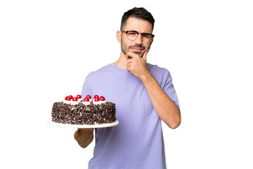 Young caucasian man holding birthday cake isolated on green chrome background thinking