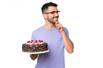 Young caucasian man holding birthday cake isolated on green chrome background looking to the side and smiling