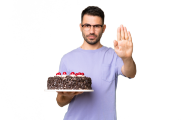 Young caucasian man holding birthday cake isolated on green chrome background making stop gesture