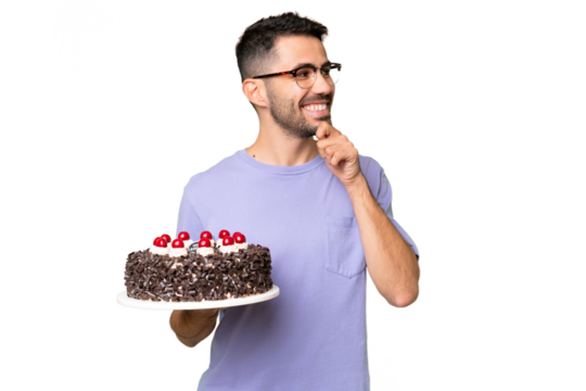 Young caucasian man holding birthday cake isolated on green chrome background looking to the side and smiling