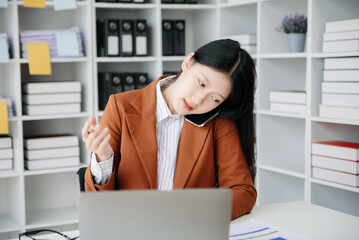 Business asian woman Talking on the phone and using a laptop with a smile while sitting in office