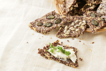 Healthy snacks from linseed, oat, herbs and various seeds, one with cream cheese and parsley garnish on a light beige napkin, copy space, selected focus