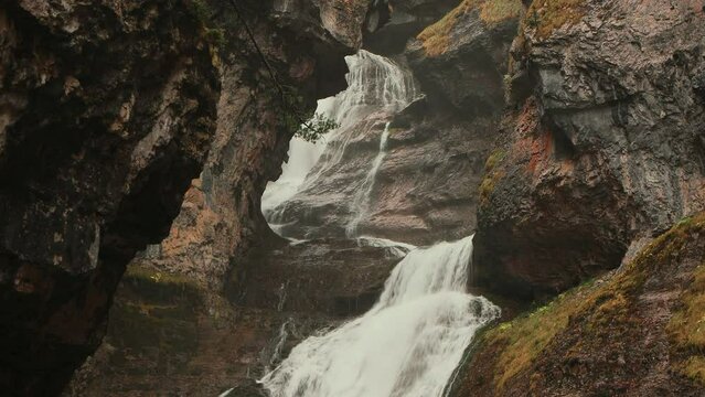 Cascada rodeada de montañas en un estrecho cañón bajo la lluvia y bruma. 