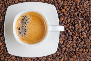 A white cup of black coffee on a background of roasted beans.