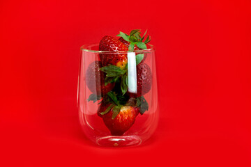 Strawberries in a glass transparent beaker with highlights close-up on a red background. Romantic background.