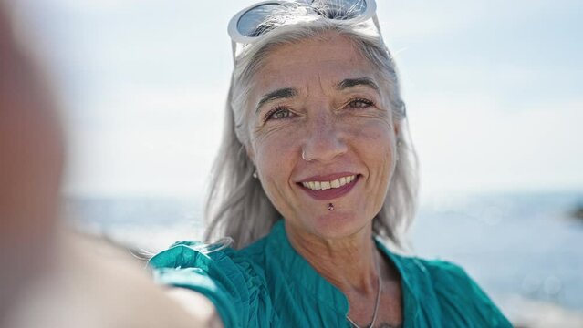 Middle age grey-haired woman tourist making selfie by the camera kissing at beach