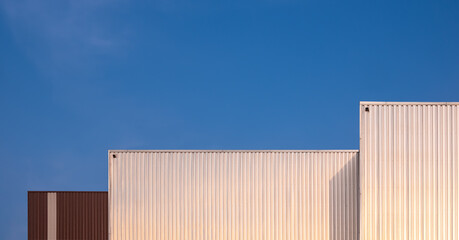 Fototapeta premium Background of 3 modern corrugated iron industrial buildings against blue clear sky