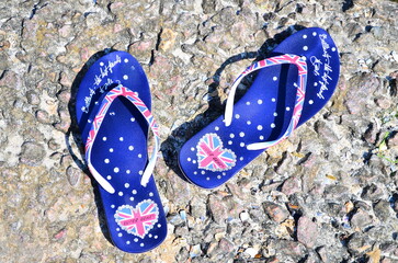 Women's, female blue flip-flops with hearts in summer, at shoreline, coastline, on rocks, stones