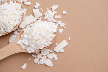 soy wax in wooden spoon on brown background, copy space