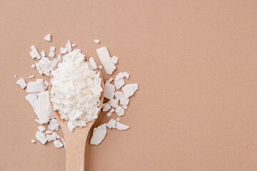 soy wax in wooden spoon on brown background, copy space