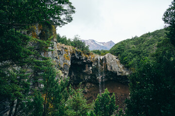View over Mangawhero Falls rushing down from 20m height of the rocks into a small river. Magnificent peaks of Mt Ruapehu behind Mangawhero Falls, Tongariro National Park, New Zealand