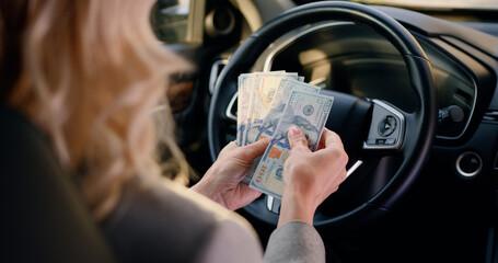 Close-up female hands behind steering wheel in luxury car counting cash financial profits in the parked car.