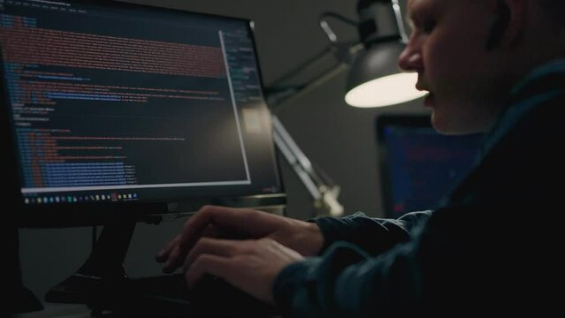 A young IT programmer works remotely in the room of his housing apartment. Programming on a laptop computer. A young man is engaged in writing program code while sitting remotely at home
