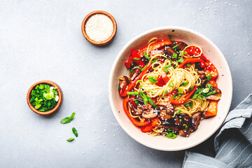 Vegan stir fry noodles with vegetables, paprika, mushrooms, chives and sesame seeds in bowl. Asian cuisine. Gray table background, top view