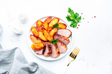 Baked pork tenderloin and quince or apple slices with parsley served on white plate. White table background, top view