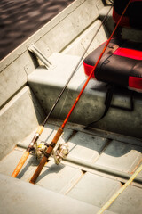 Two fishing poles lean on the padded red & black seat in this aluminum flat-bottomed fishing row boat. Poles are at the ready this spring as it warms and the fish start biting.