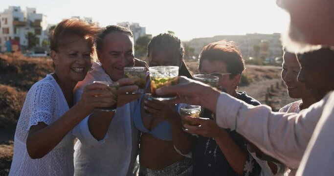 Senior multiracial friends cheering with alcohol free mojitos on the beach - Mature people having fun during summer vacation at sunset