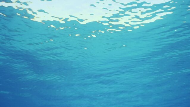 Small swell on surface of Ocean, Slow motion. Surface of water during calm on sunny day. Underwater view of calm blue water surface. Natural blue water background. Beautiful clear blue water surface