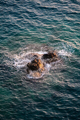 A stone from the water under the rays of the sun, against which the blue waves of the sea beat with a splash and foam