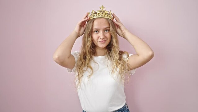 Young blonde woman smiling confident wearing princess crown over isolated pink background