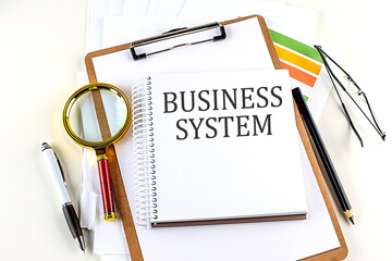 BUSINESS SYSTEM text on notebook with clipboard on white background