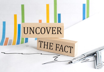 UNCOVER THE FACT text on a wooden block on chart background, business concept