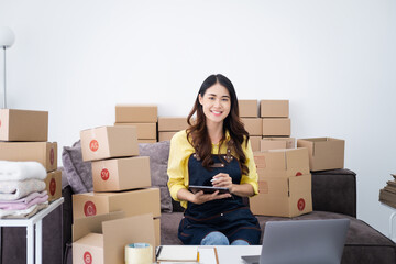 Startup small business, A young Asian woman checking online order on digital tablet and packing boxes for products to send to customers. working at the home office.