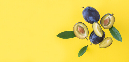 Flying in air fresh ripe whole and cut blue plums with leaves on the yellow background. Copy space. Top view.