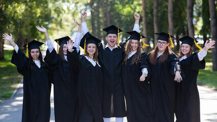 Group of happy graduates in robes outdoors. 