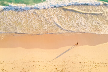 Overhead view of alone man walking by the white sandy beach along the amazing clear light blue ocean. Aerial view of a walking man on a beach, lonely on the sand with beautiful view of waves.