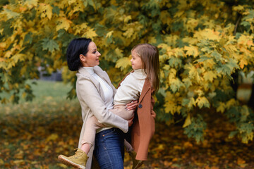 little beautiful girl with her mother hugging and kissing in the park in autumn in golden leaves
