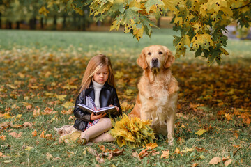 little beautiful girl in the park in autumn in golden leaves with a dog golden retriever labrador hugs and rejoices