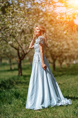 Blond garden. Portrait of a blonde in the park. Happy woman with long blond hair in a blue dress.