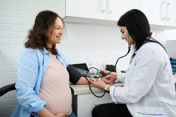 Female Obstetrician gynecologist doctor measuring blood pressure of the pregnant woman in the hospital. Pregnancy-induced Hypertension and prophylaxis of eclampsia and preeclampsia concept. Gynecology - obrazy, fototapety, plakaty