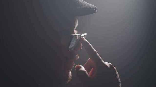 Night cinematic portrait of handsome entrepreneur retro English man with cap and beard fitting his flasses in slow motion