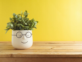 Cute funny plant on wooden table over yellow background. Home or office decoration concept