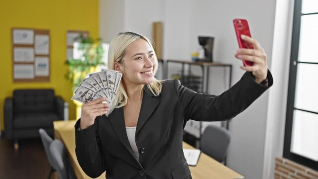 Young beautiful hispanic woman business worker holding dollars make selfie by smartphone at office