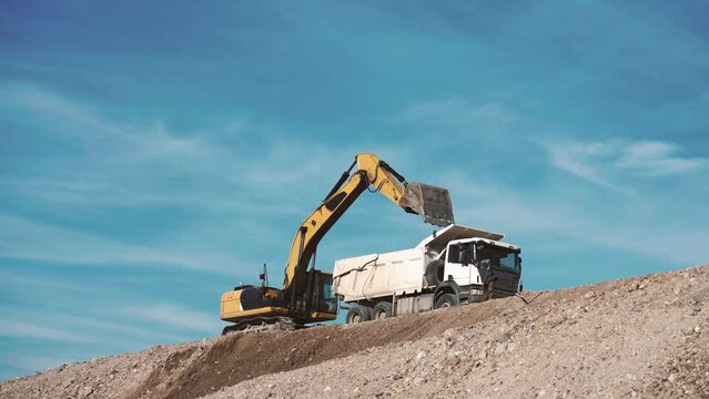 Crawler excavator digger loading earth gravel on transportation truck at road construction site, slow motion