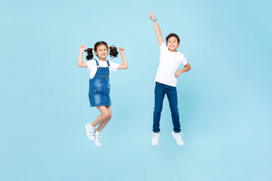 Mixed race Asian boy and girl playing by jumping in the air against light blue color isolated background studio shot