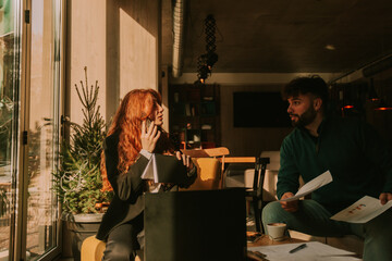 Ginger female worker talking to her male colleague while having a phone fall