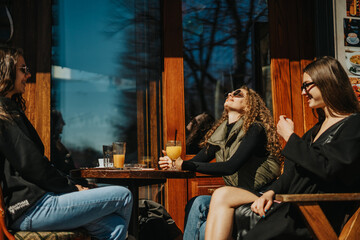 Two girls having fun conversation while their curly haired friend is enjoying the sun rays. They are sitting at the coffee bar