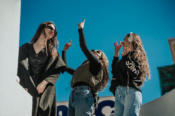 Three lovely happy girls having fun out in the city on a beautiful sunny day. They are listening to music and dancing