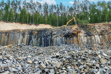 Basalt mining. Excavators in a basalt quarry near the forest.
