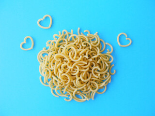 Uncooked curly pasta with heart shaped noodles on blue background top view        