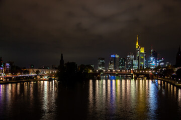 Fototapeta na wymiar of Frankfurt's illuminated skyline, bridge traffic, and city lights reflecting on the river during a partly cloudy autumn night.