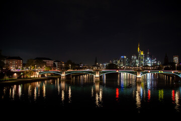 "Night  of Frankfurt, Germany with river, bridge, traffic, city illumination reflected in water, and downtown skyline with skyscrapers in autumn."