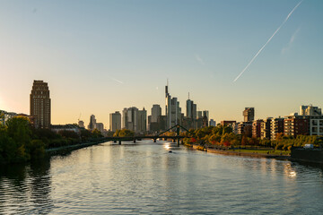 Obraz premium Stunning of Frankfurt's downtown skyline with a bridge, river reflections, and skyscrapers at sunset. Clear autumn sky and vibrant cityscape.