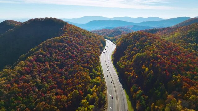 Aerial view of I-40 freeway in North Carolina heading to Asheville through Appalachian mountains in golden fall with moving trucks and cars. Interstate transportation concept