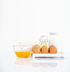 Wheat flour with eggs, oil and milk on table . White table Front view copyspace