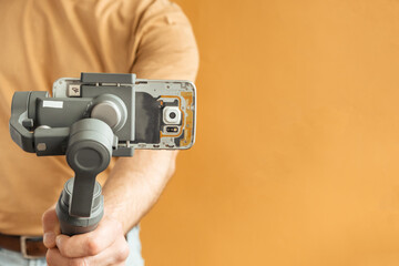 Man filming with a smartphone using a gimbal stabilizer on yellow background. Using three-axis electronic stabilizer to make vlogs or video shooting.